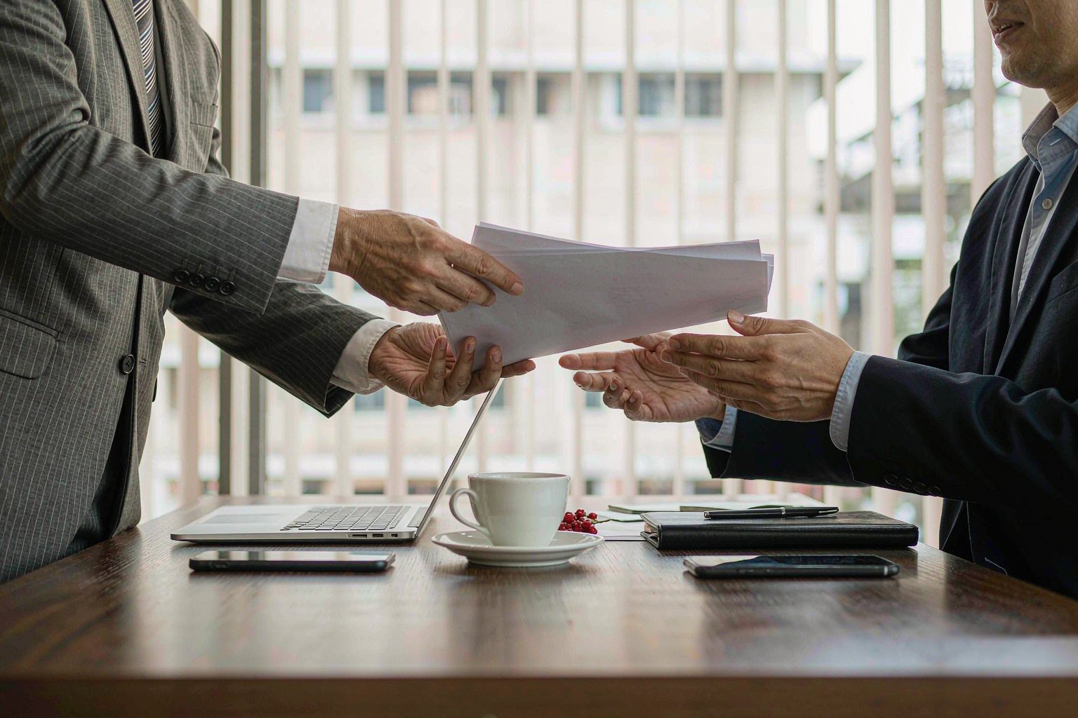 Buyer and supplier representatives exchanging documents in a meeting room