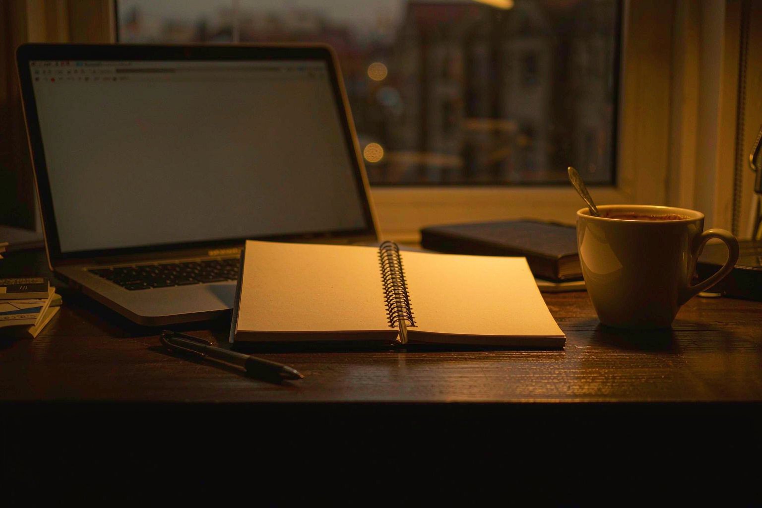 Notebook, laptop and coffee on a desk during an evening research session
